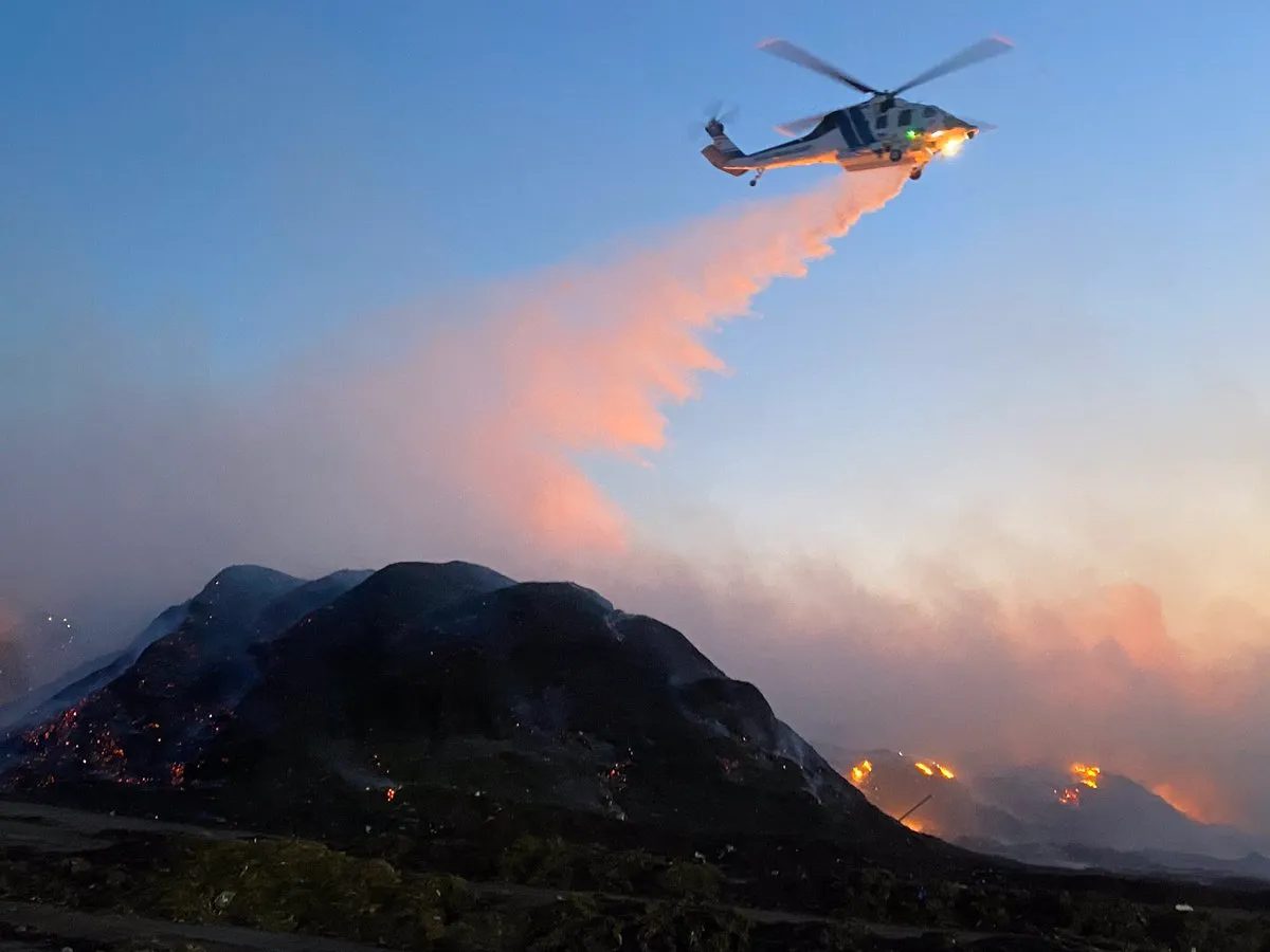 A firefighting helicopter making a water drop on a hillside fire at dusk